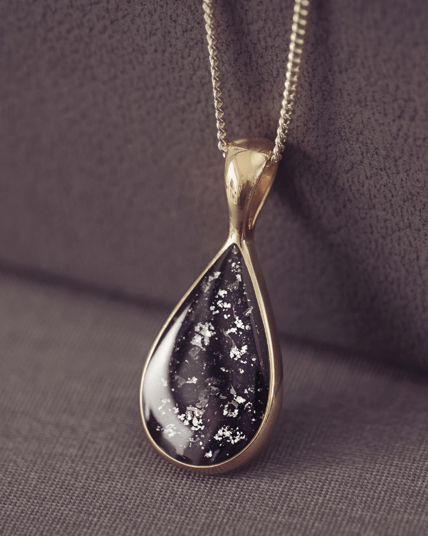 Teardrop-shaped pendant crafted in 9 carat gold on a dark fabric background