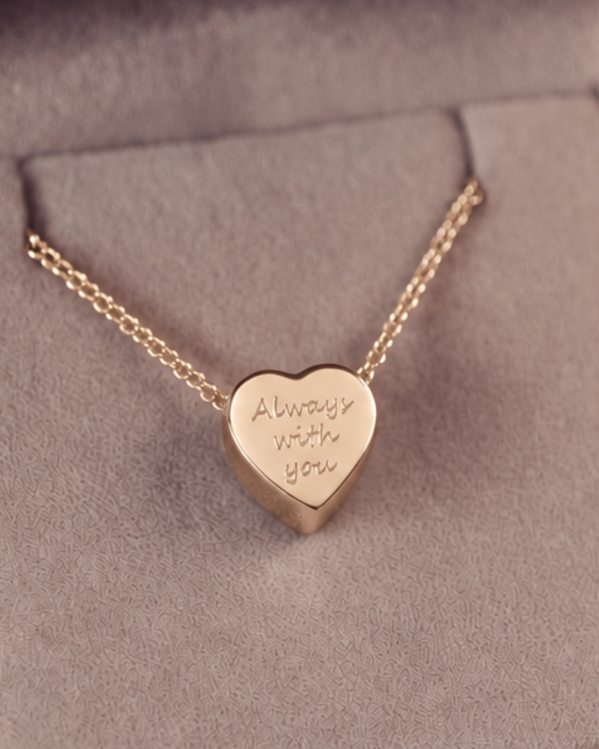 A gold heart-shaped pendant necklace engraved with 'Always with you' on a textured gray jewelry box.