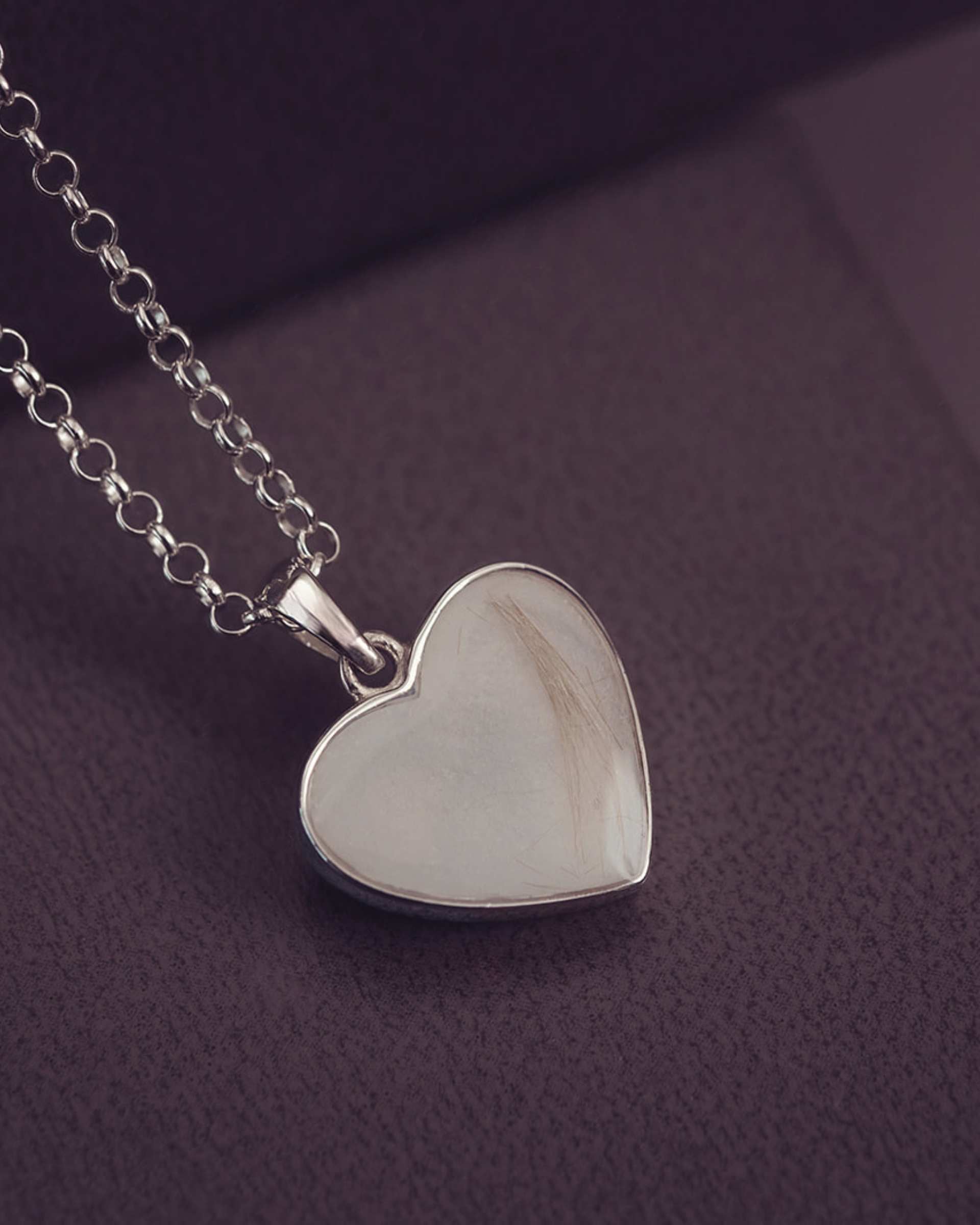 Silver heart-shaped pendant on a chain against a dark purple background