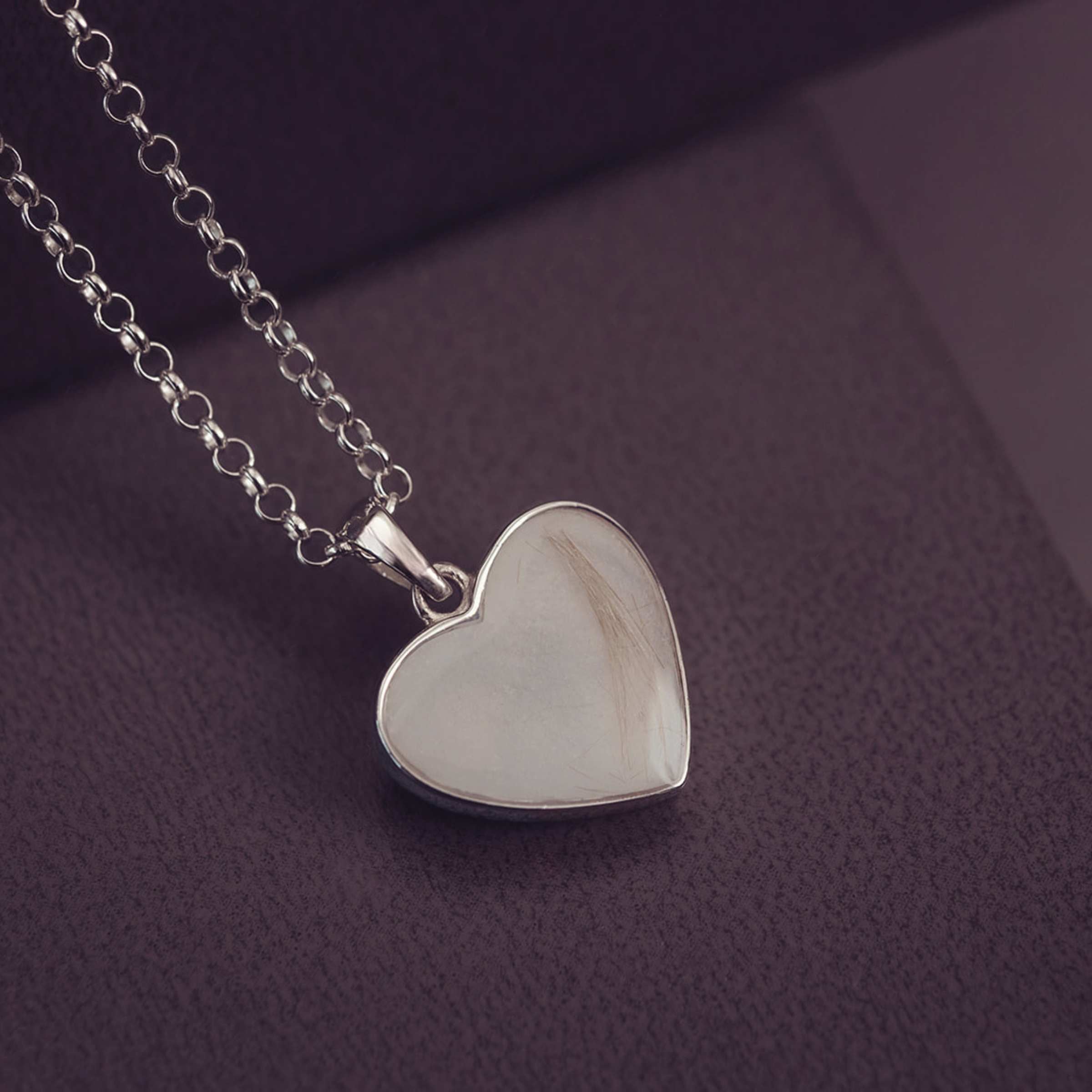 Silver heart-shaped pendant on a chain against a dark purple background