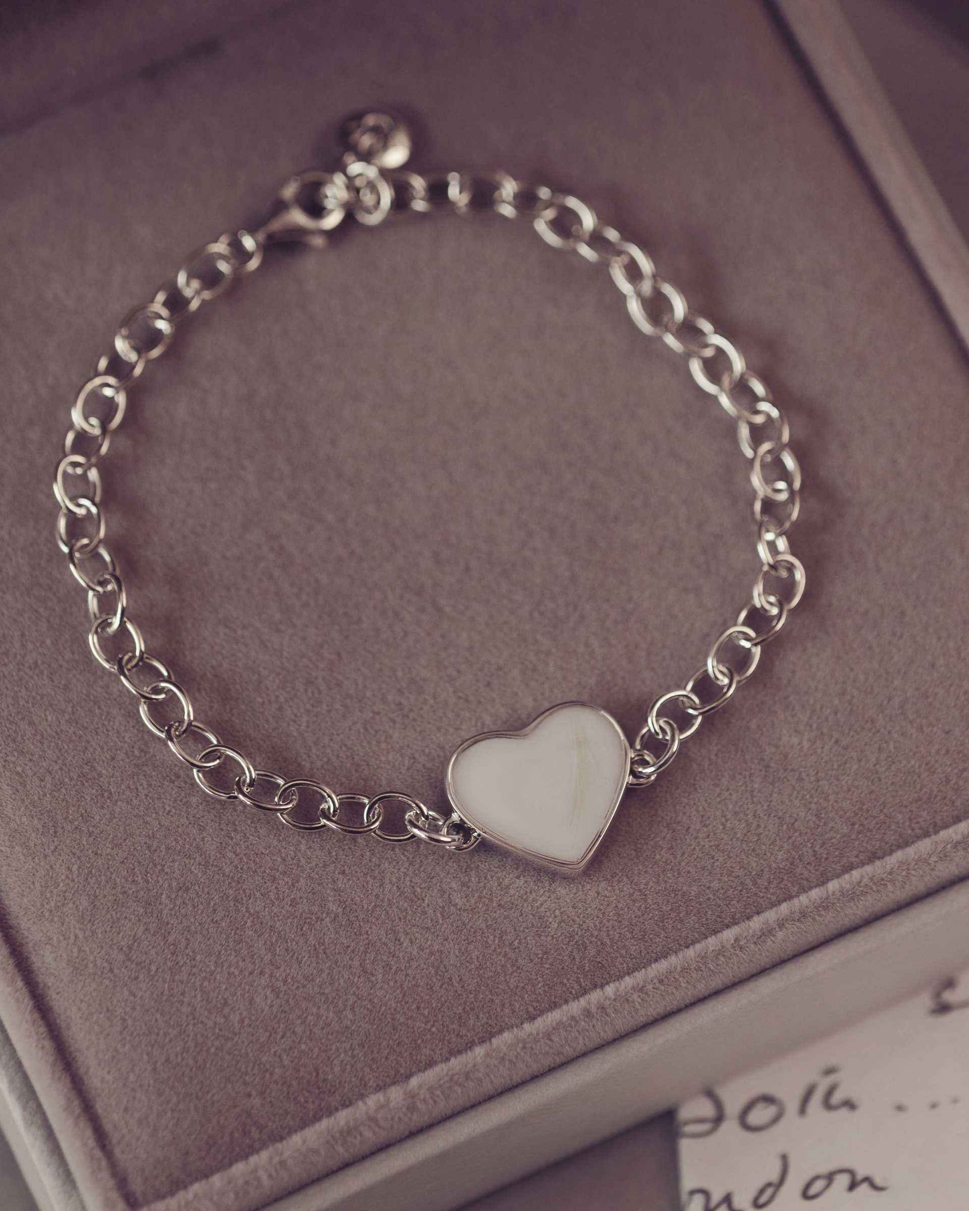 Silver chain bracelet with a heart-shaped charm on a soft surface