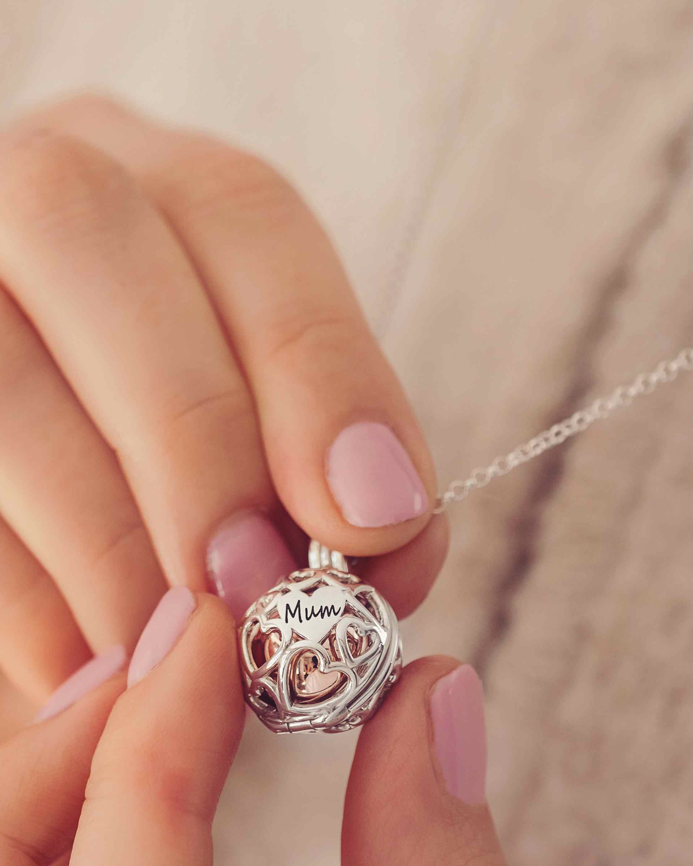 A Silver and gold round locket with the word Mum engraved held in a ladies hands