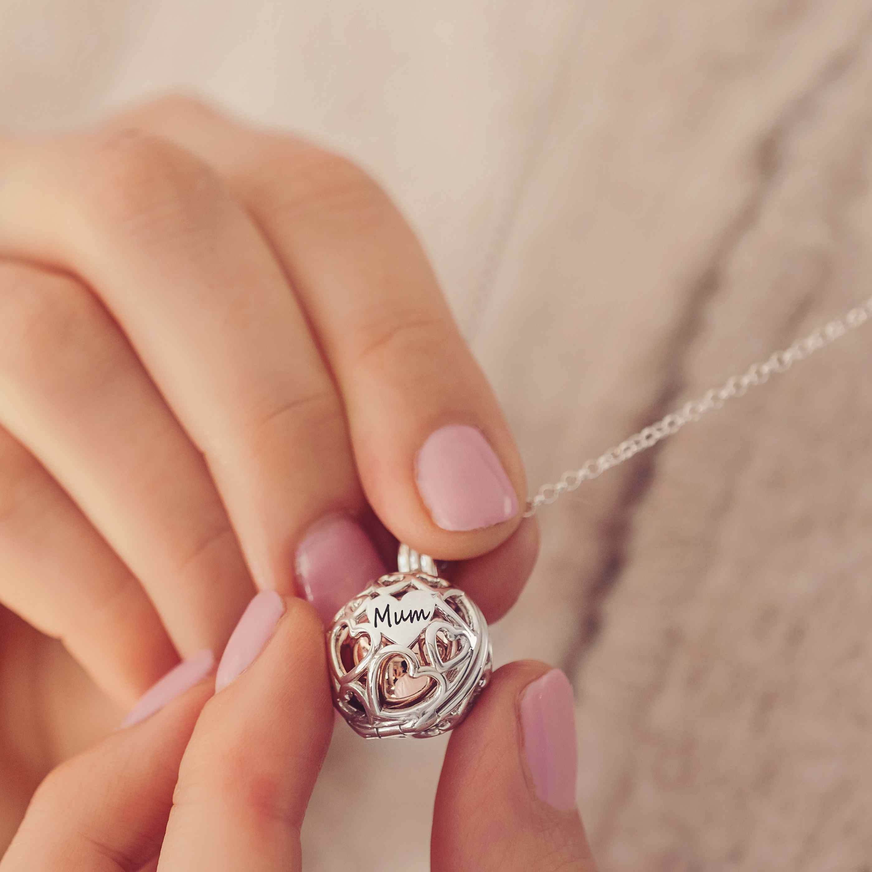 A Silver and gold round locket with the word Mum engraved held in a ladies hands