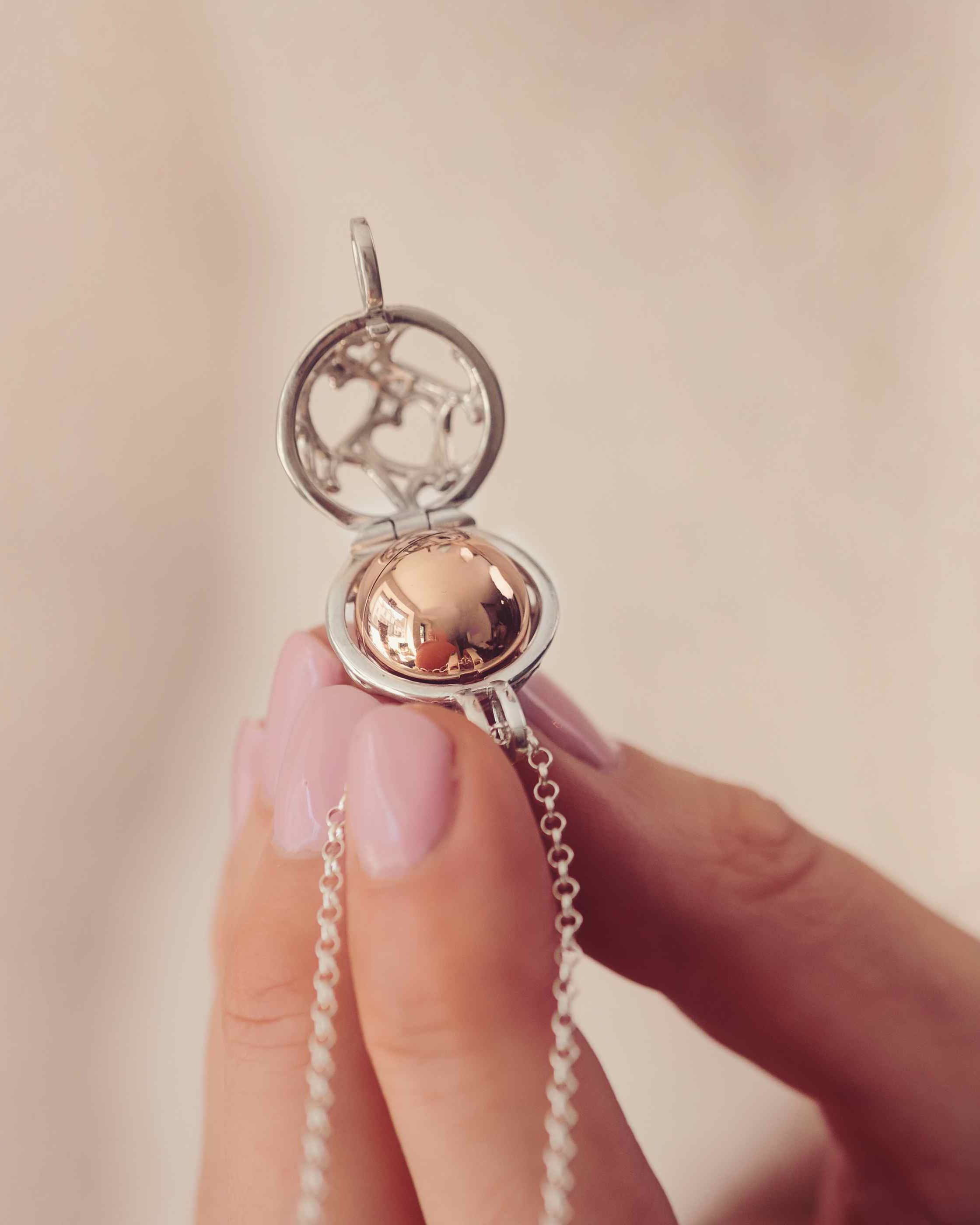 A Silver and gold round locket with the word Mum engraved held in a ladies hands