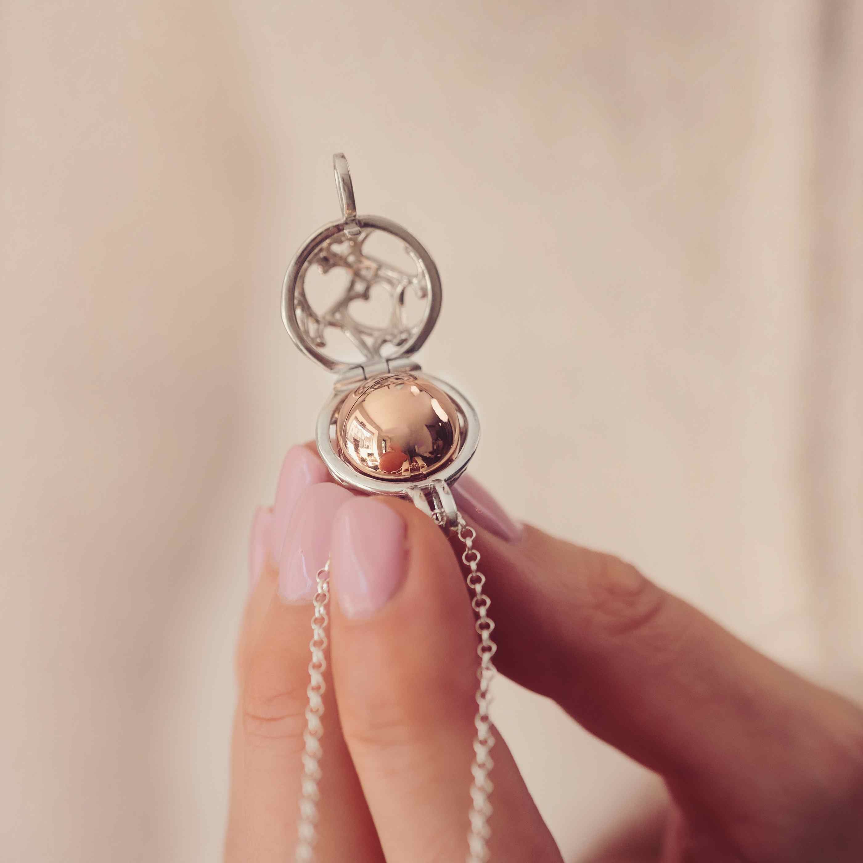 A Silver and gold round locket with the word Mum engraved held in a ladies hands