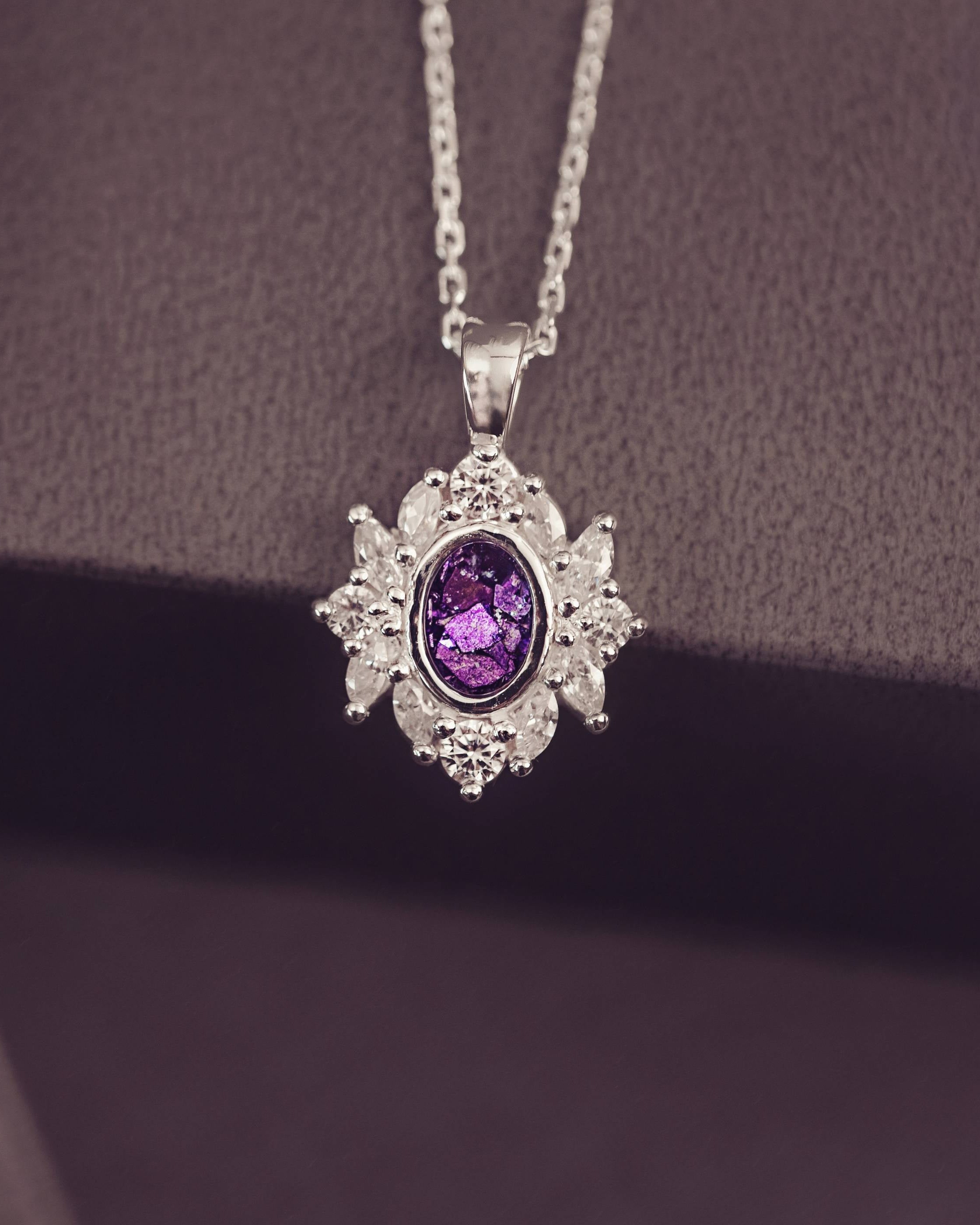 Silver pendant with a purple gemstone on a chain against a dark background