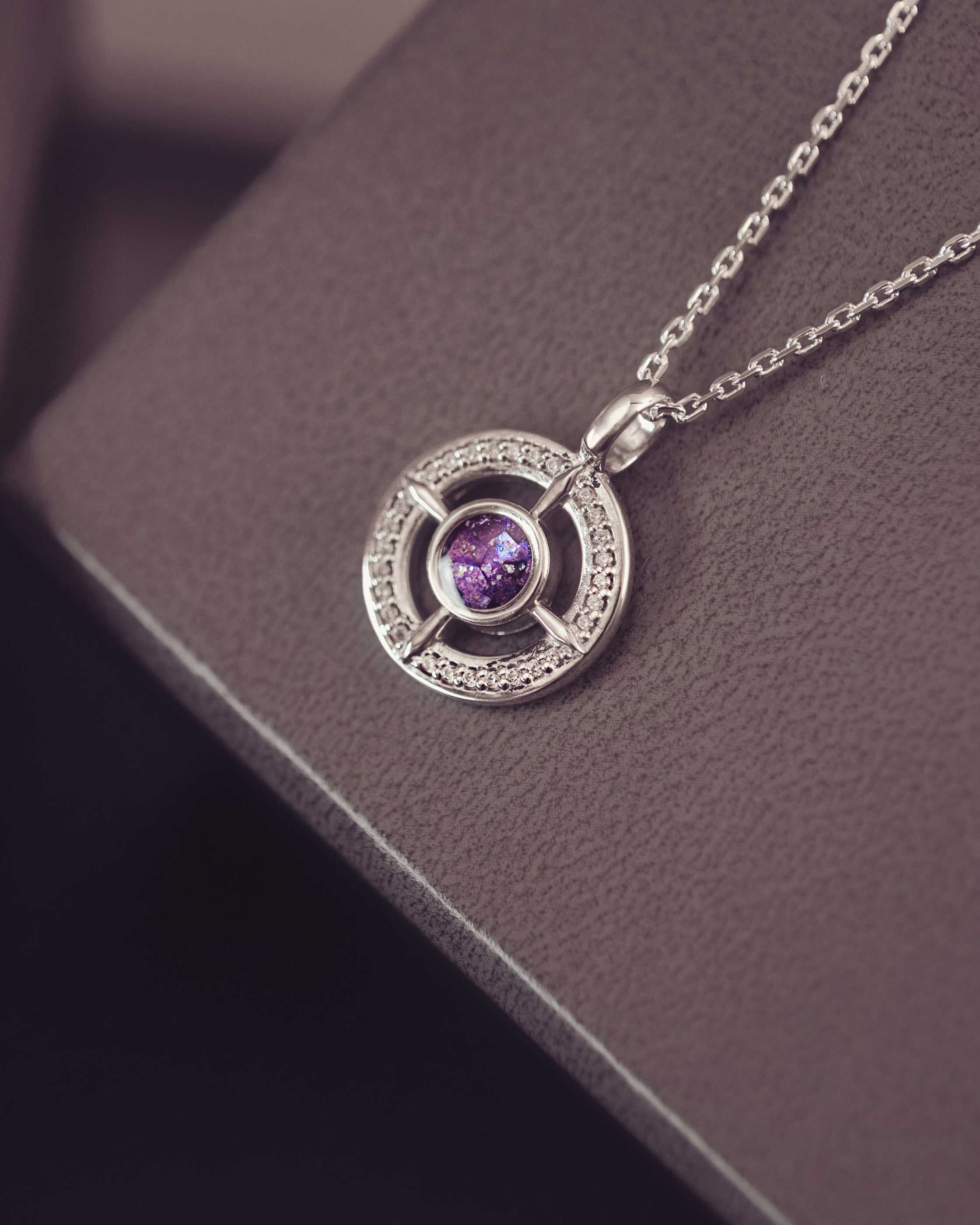 Silver necklace with a purple gemstone pendant on a dark surface