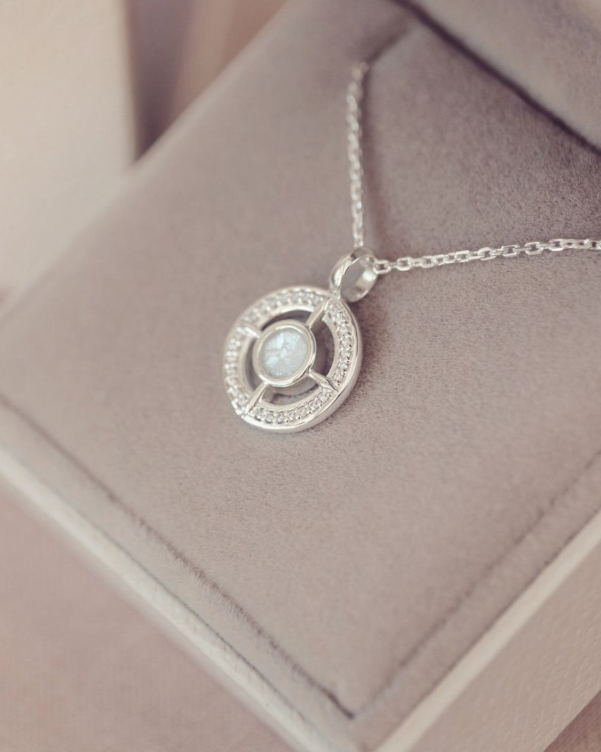 Silver necklace with a circular pendant on a soft pink surface
