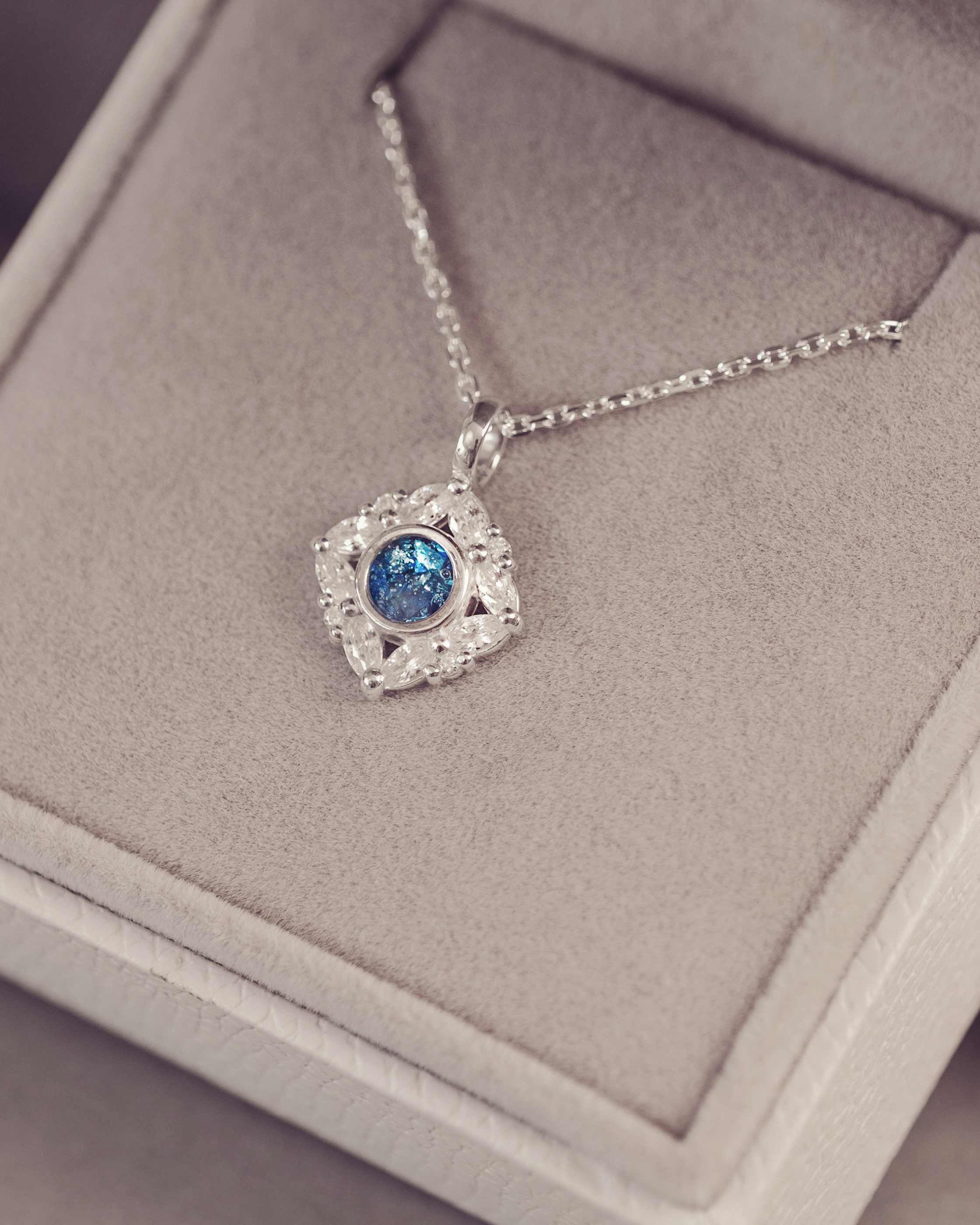 Silver necklace with a blue gemstone pendant on a gray cushion