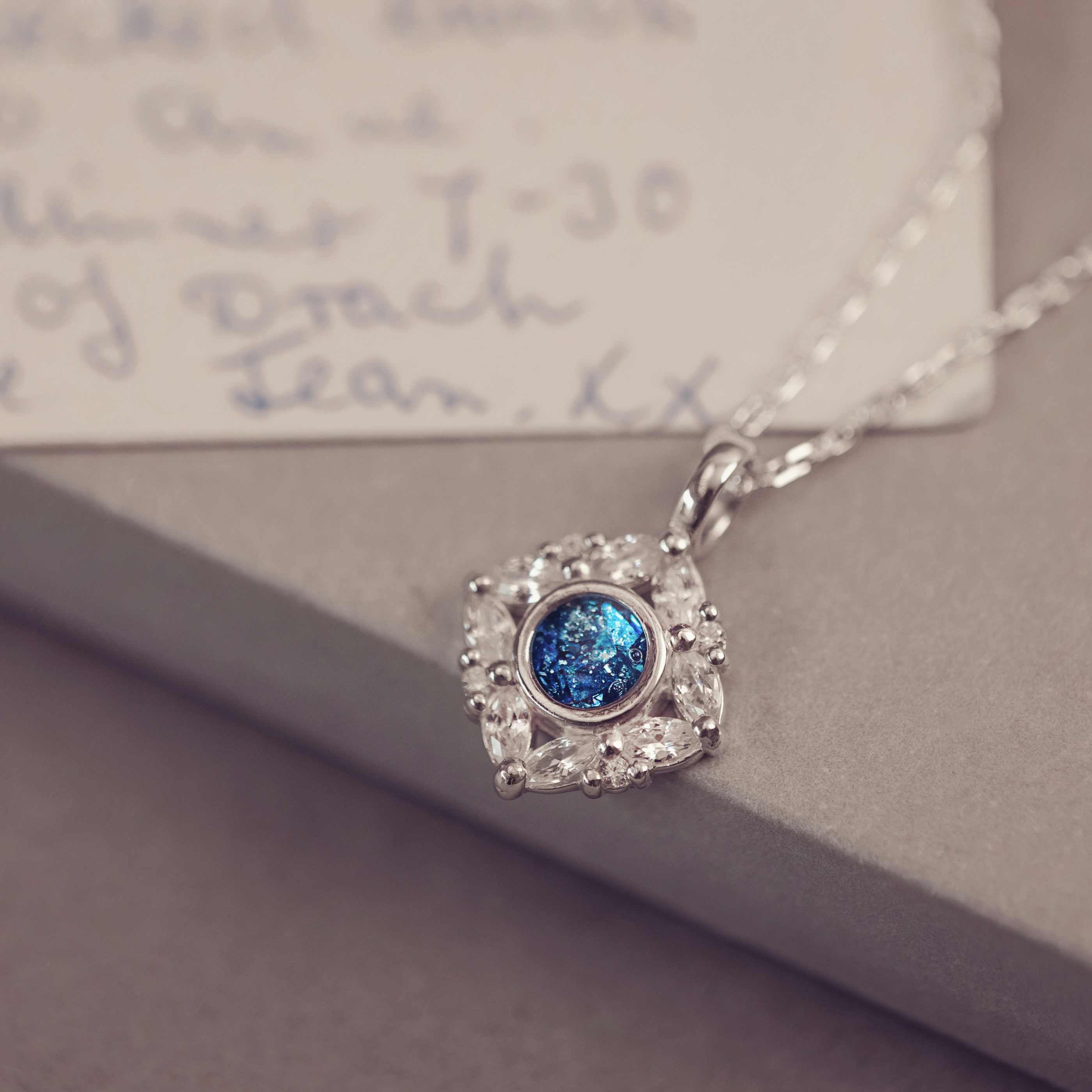 Silver necklace with a blue gemstone pendant on a textured surface