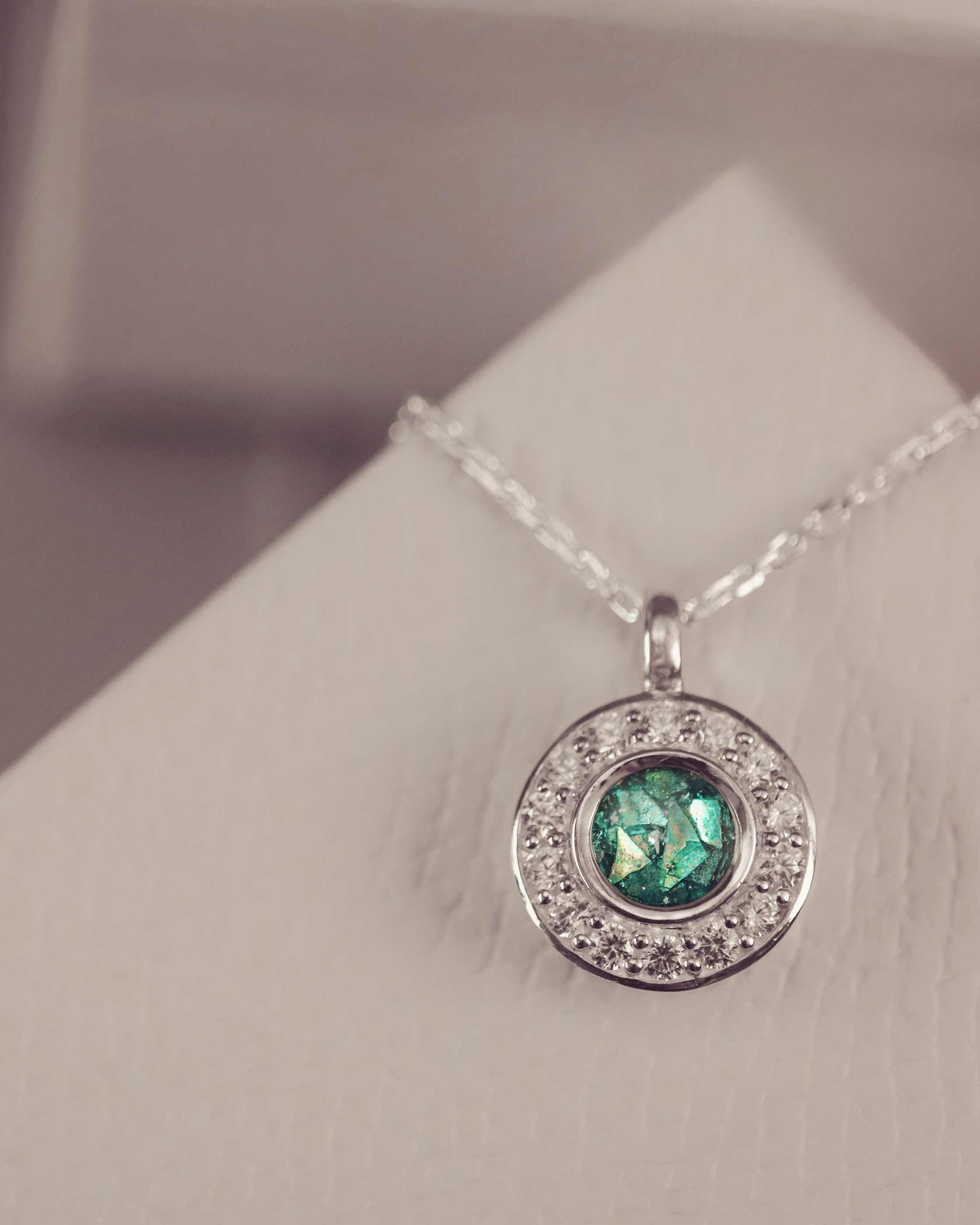 Silver necklace with a green gemstone pendant on a white stand.