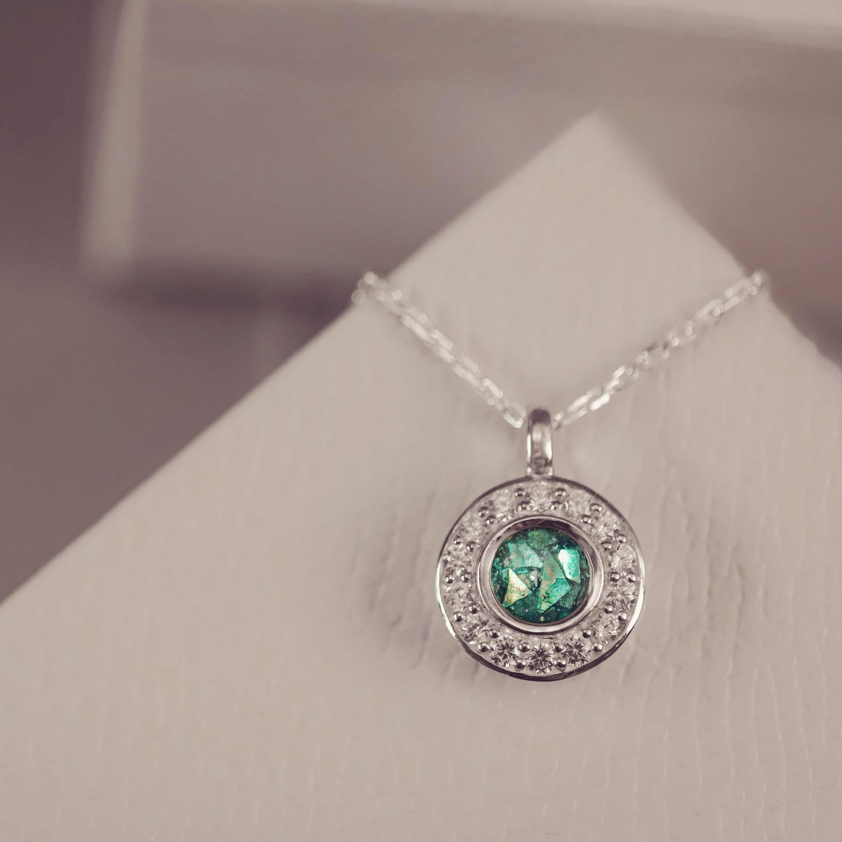 Silver necklace with a green gemstone pendant on a white stand.