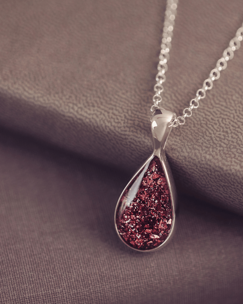 Sterling silver teardrop necklace with a central section filled with memorial ashes and brown crushed crystals, displayed on dark background