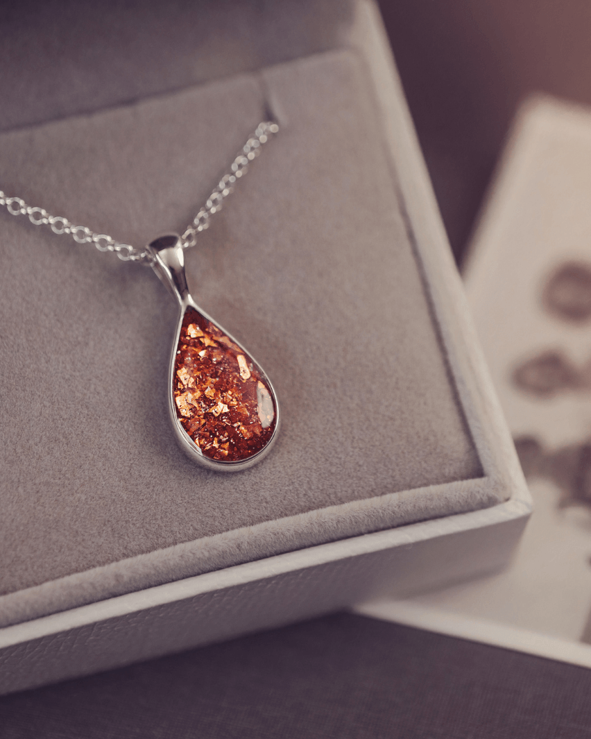 Sterling silver teardrop necklace with a central section filled with memorial ashes and orange crushed crystals, displayed in a grey jewellery box