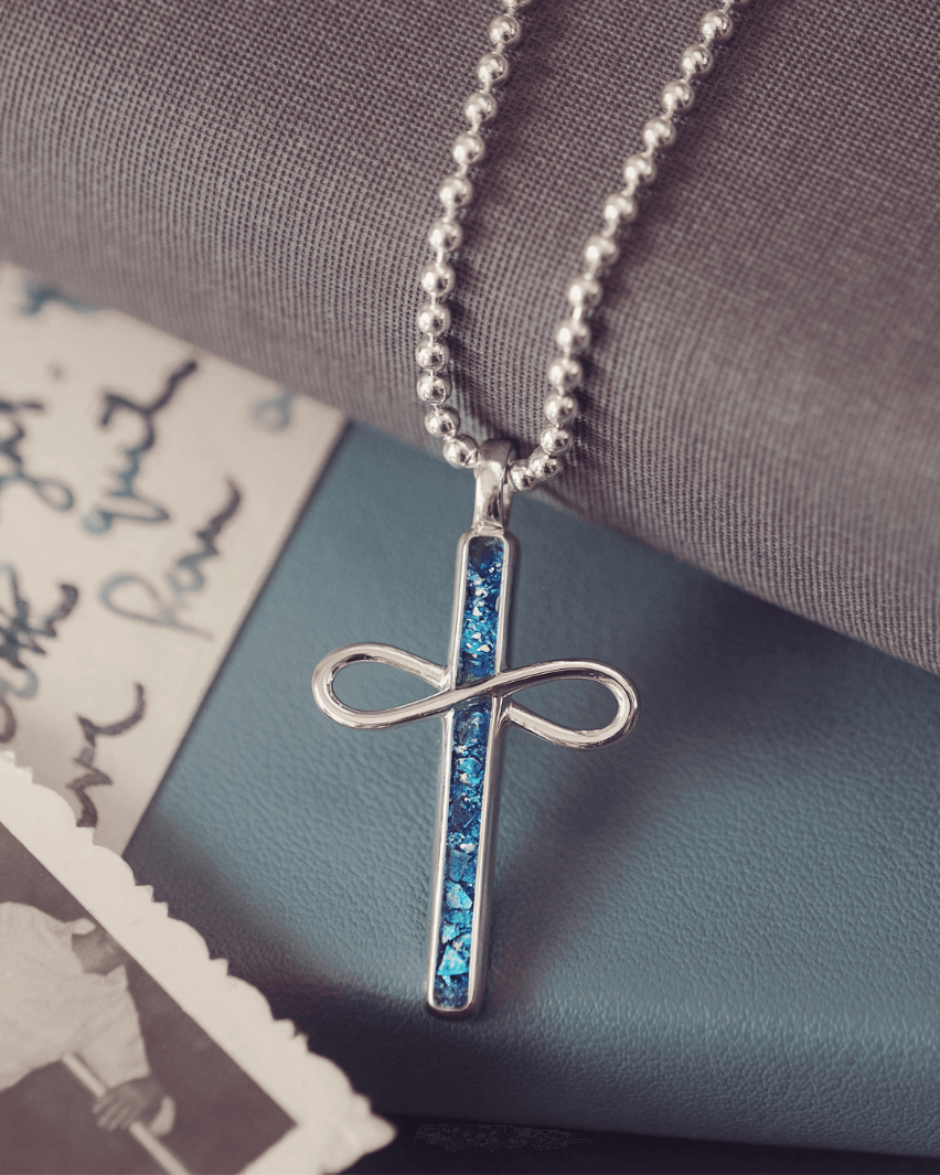 Silver cross pendant necklace with blue accents on a textured surface