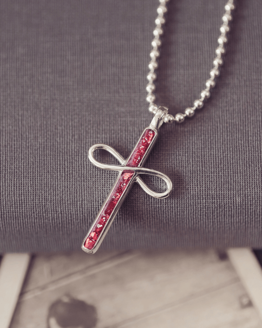 Silver cross pendant with red stones on a chain against a gray background