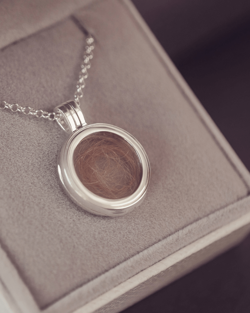 Round silver locket necklace with acrylic showing a locket of hair inside on a textured surface