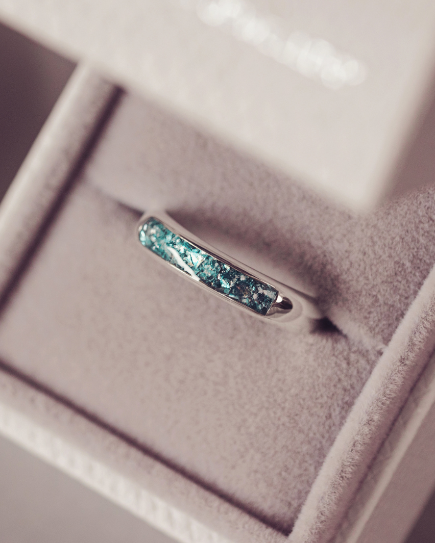 A silver band ring with a textured, crackled turquoise blue inlay, displayed inside an open light beige jewelry box.