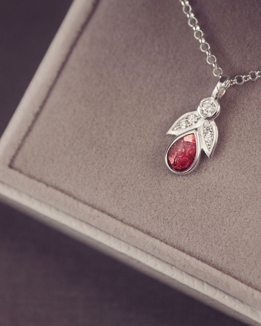 Silver necklace with a red teardrop pendant on a gray surface