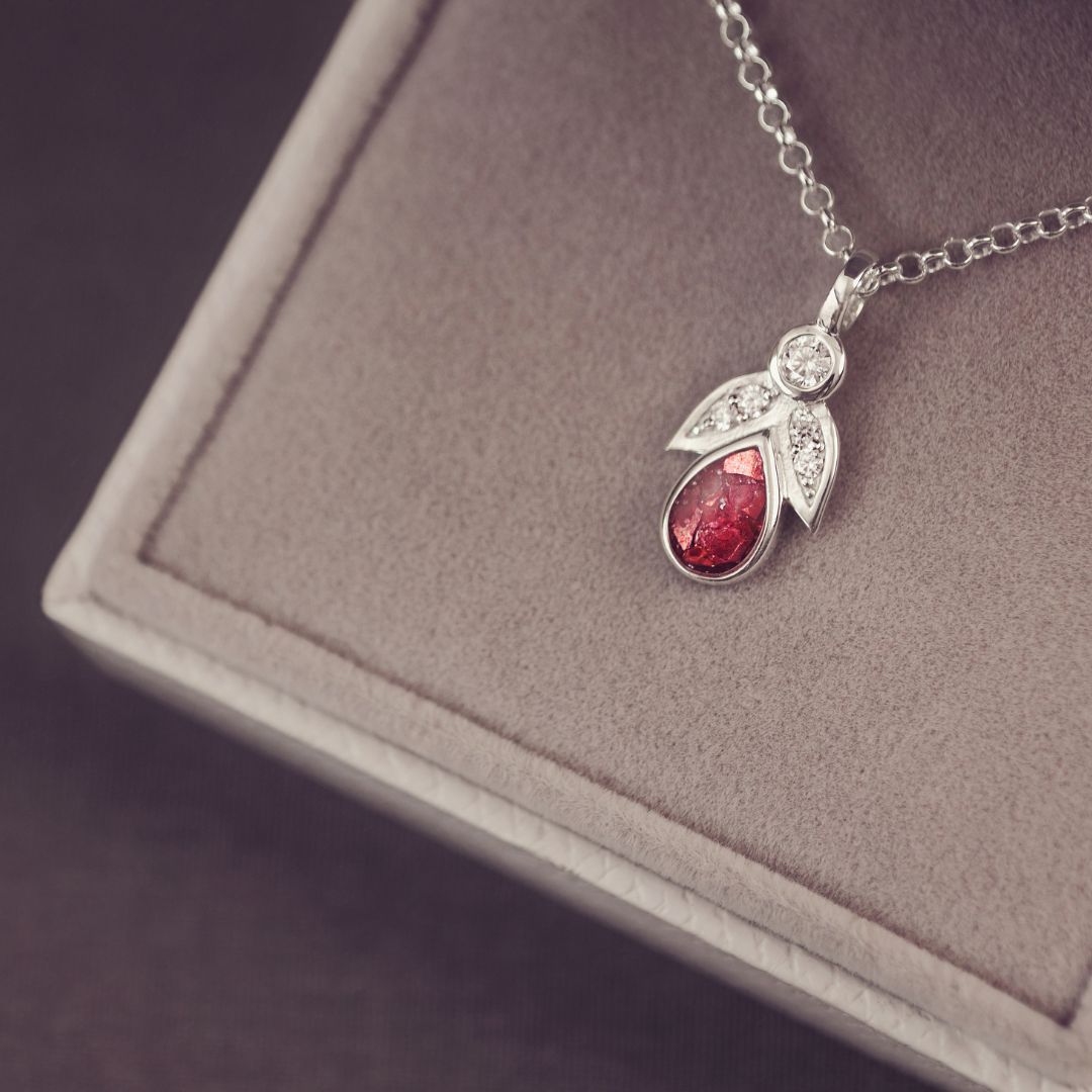 Silver necklace with a red teardrop pendant on a gray surface