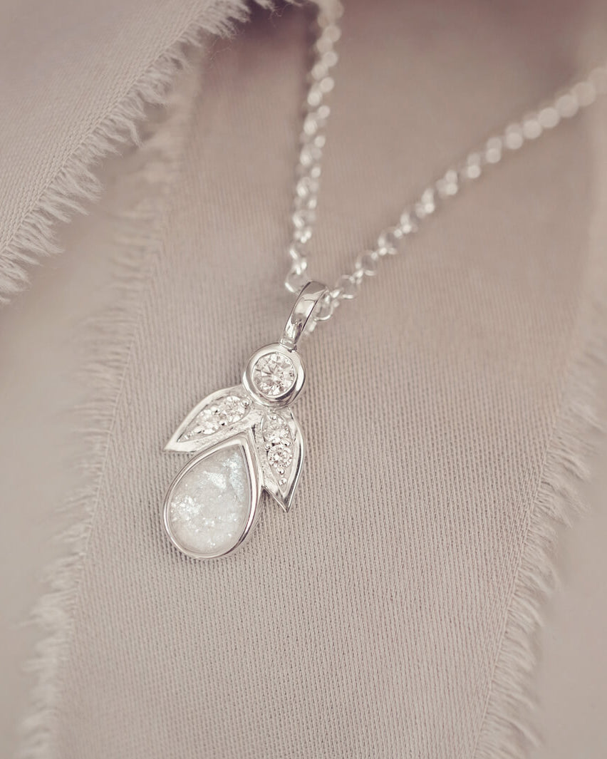 sterling silver angel pendant with clear floating crystals sat on a cream fabric