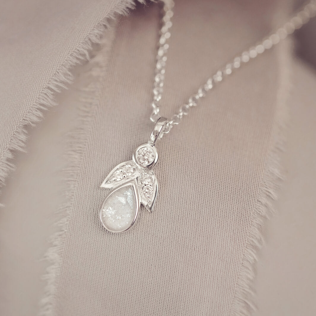sterling silver angel pendant with clear floating crystals sat on a cream fabric