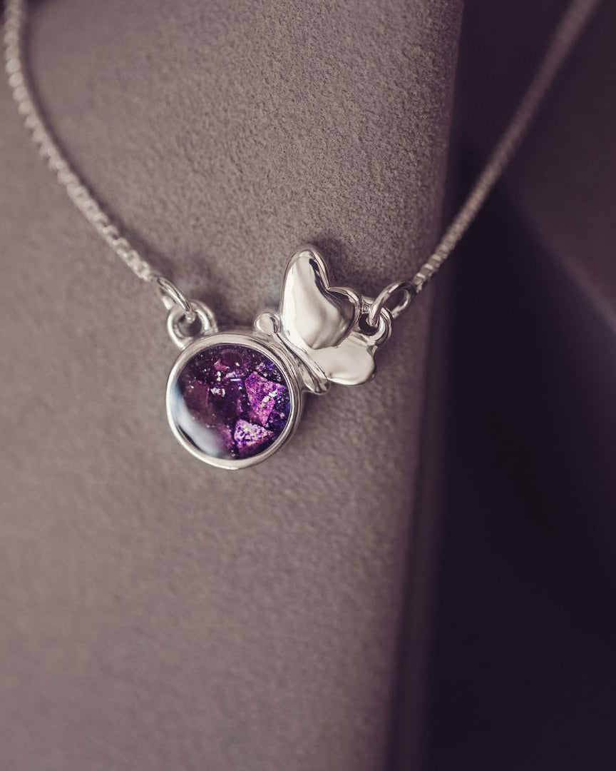 Necklace with a purple pendant and silver butterfly charm on a neutral background