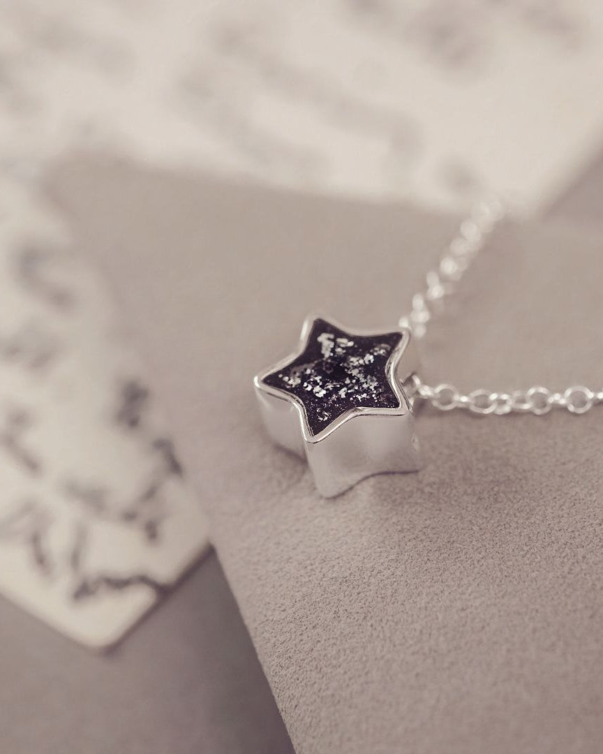 Silver star-shaped pendant on a chain against a neutral background