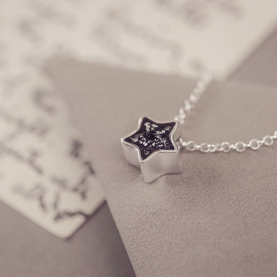 Silver star-shaped pendant on a chain against a neutral background