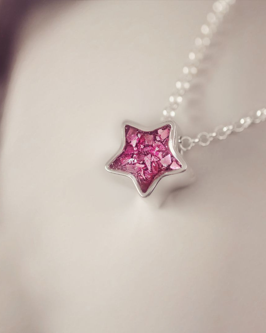 Star-shaped pink gemstone pendant on a chain against a neutral background