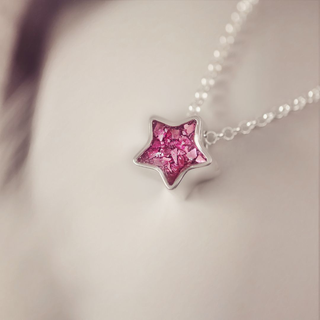 Star-shaped pink gemstone pendant on a chain against a neutral background