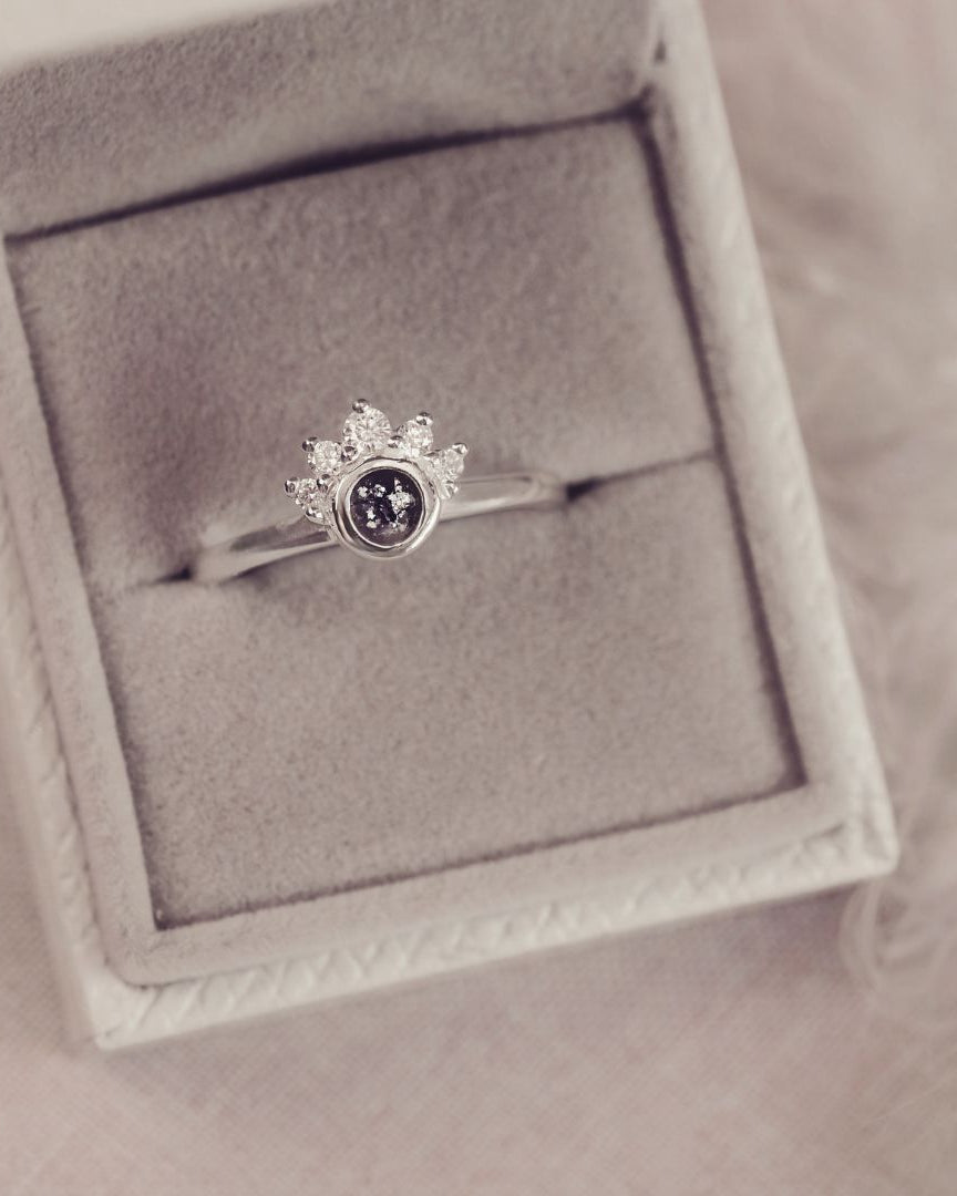 Silver ring with a central gemstone in a gray jewelry box