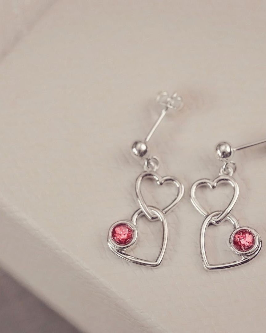 Two silver heart dangle earrings with red gemstones