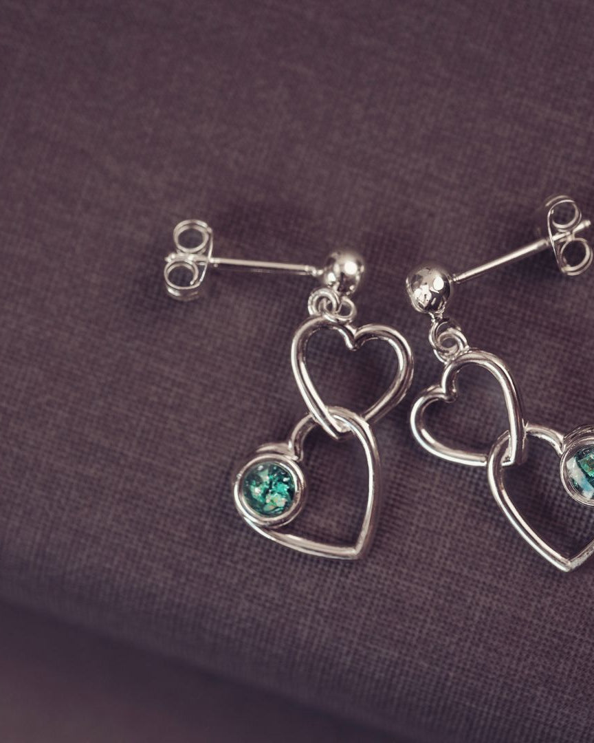 two silver heart earrings on a dark purple background with green gemstones