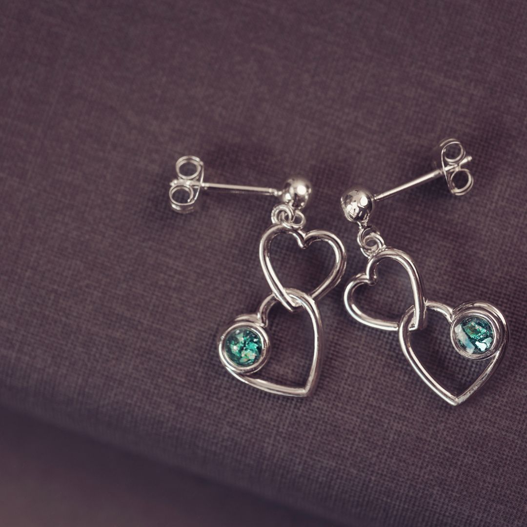 two silver heart earrings on a dark purple background with green gemstones