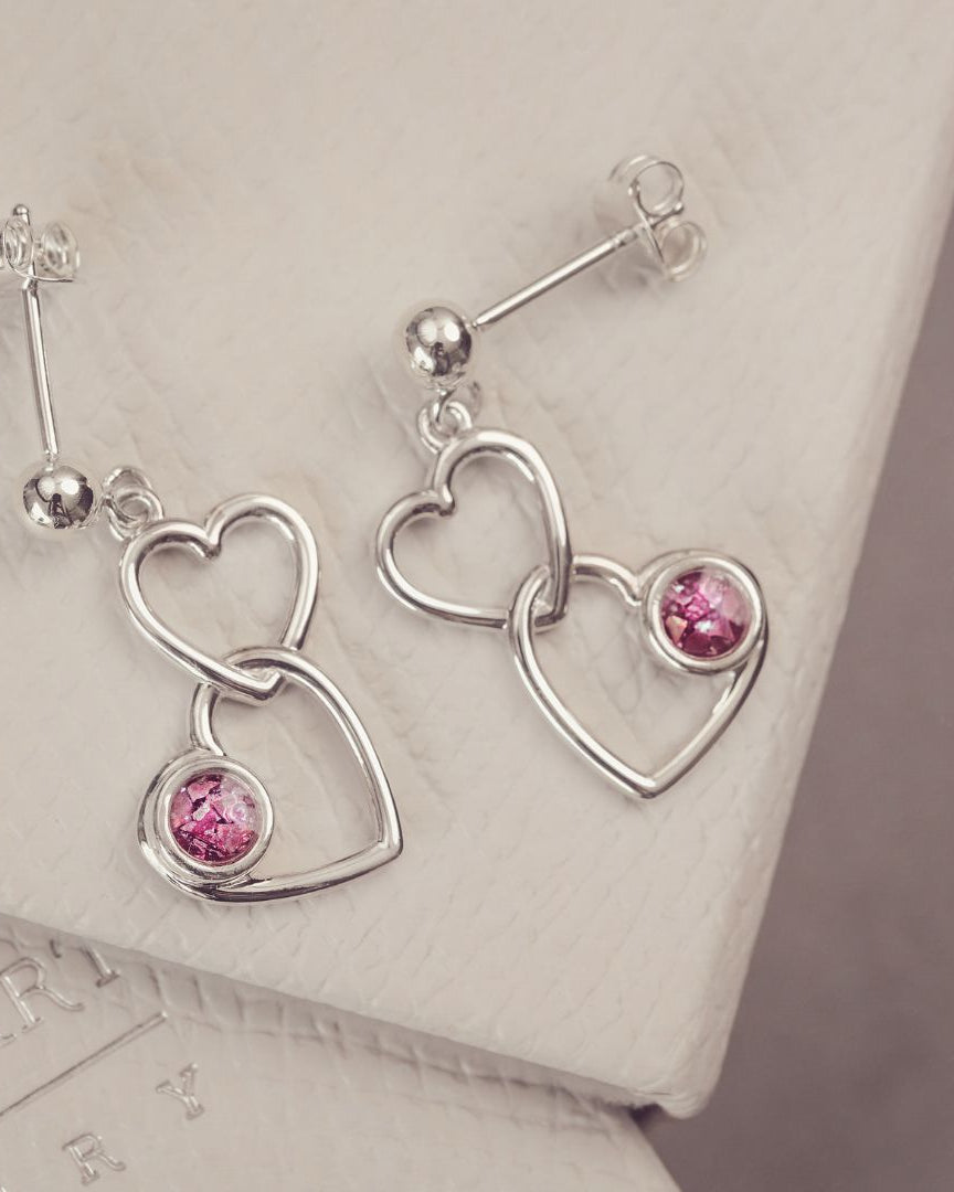 two silver heart earrings with pink gemstones on a grey background