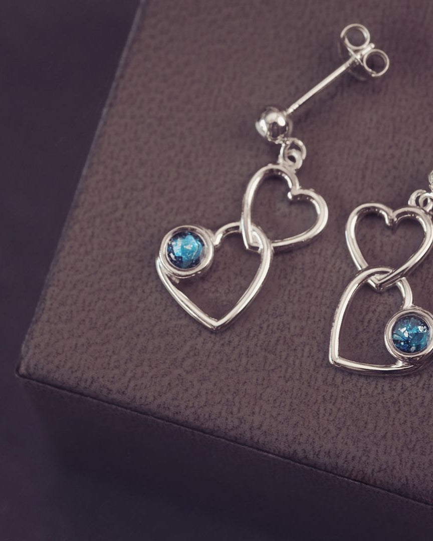 two silver heart dangle earrings with blue genstones on a dark purple background