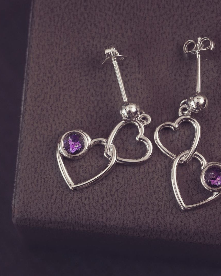 two silver heart dangle earrings with purple genstones on a dark purple background
