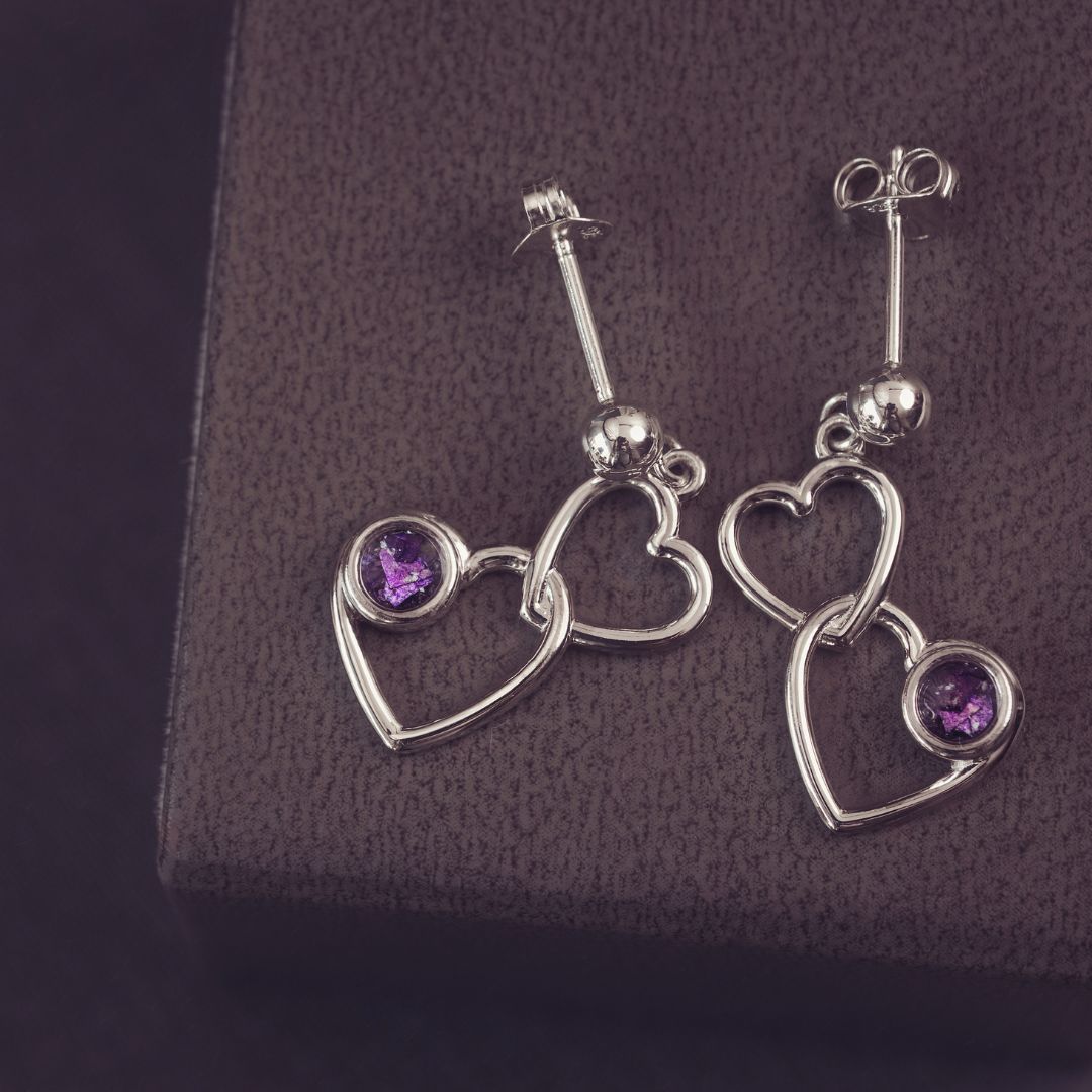 two silver heart dangle earrings with purple genstones on a dark purple background