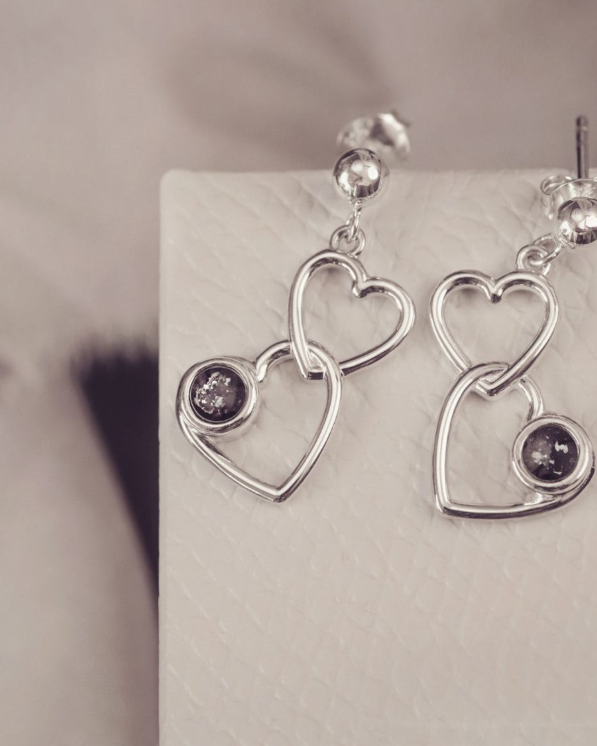 two silver heart dangle earrings with black gemstones on a silver and grey background