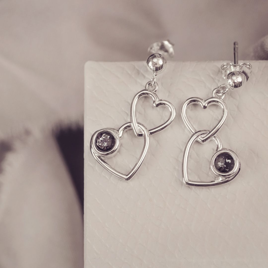 two silver heart dangle earrings with black gemstones on a silver and grey background