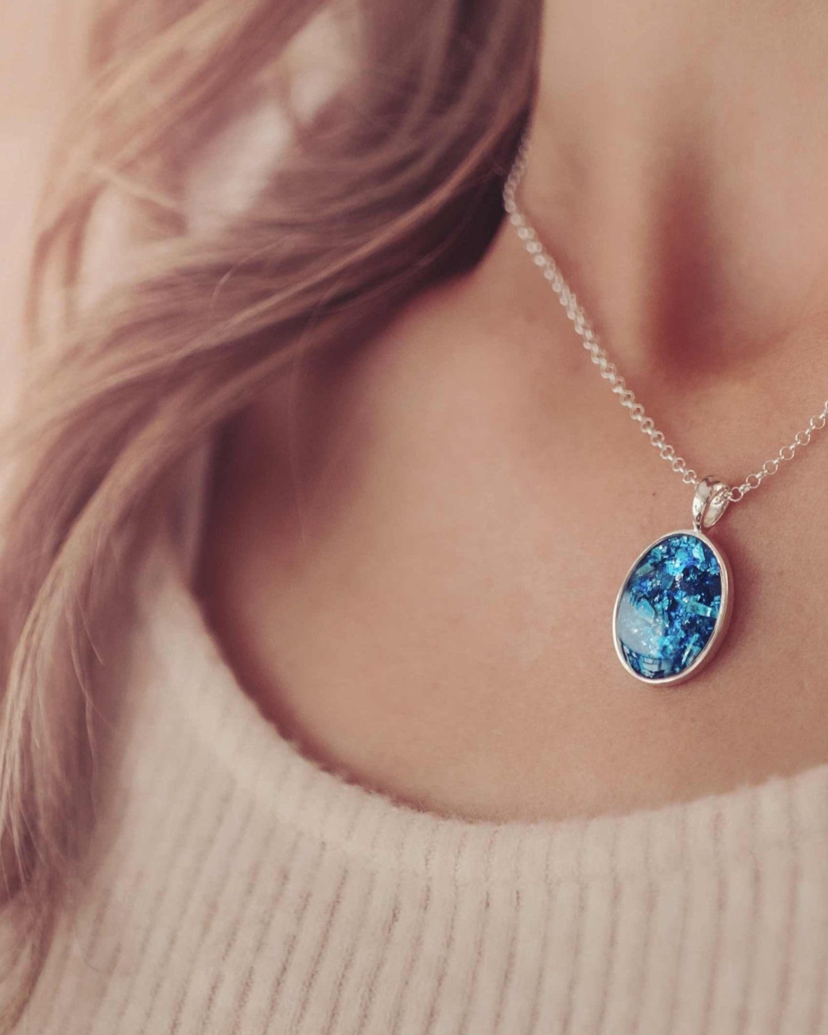 A lady's neckline showing a silver and blue oval cremation ashes necklace.