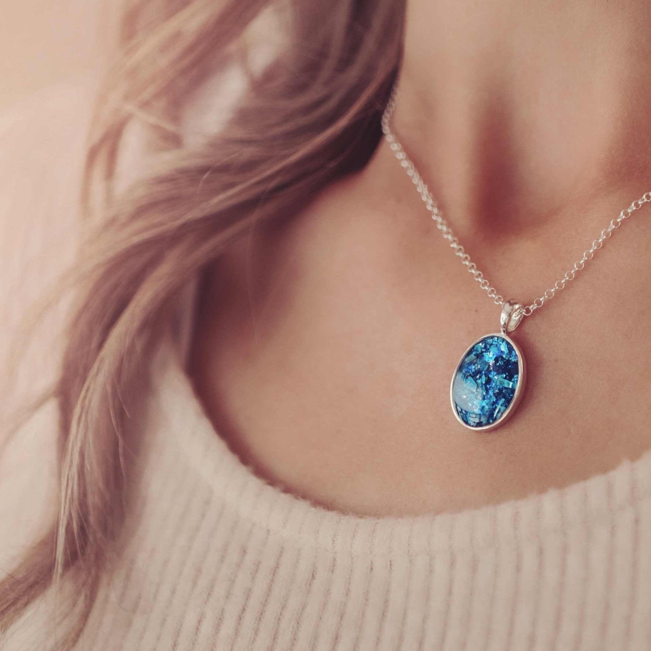 A lady's neckline showing a silver and blue oval cremation ashes necklace.