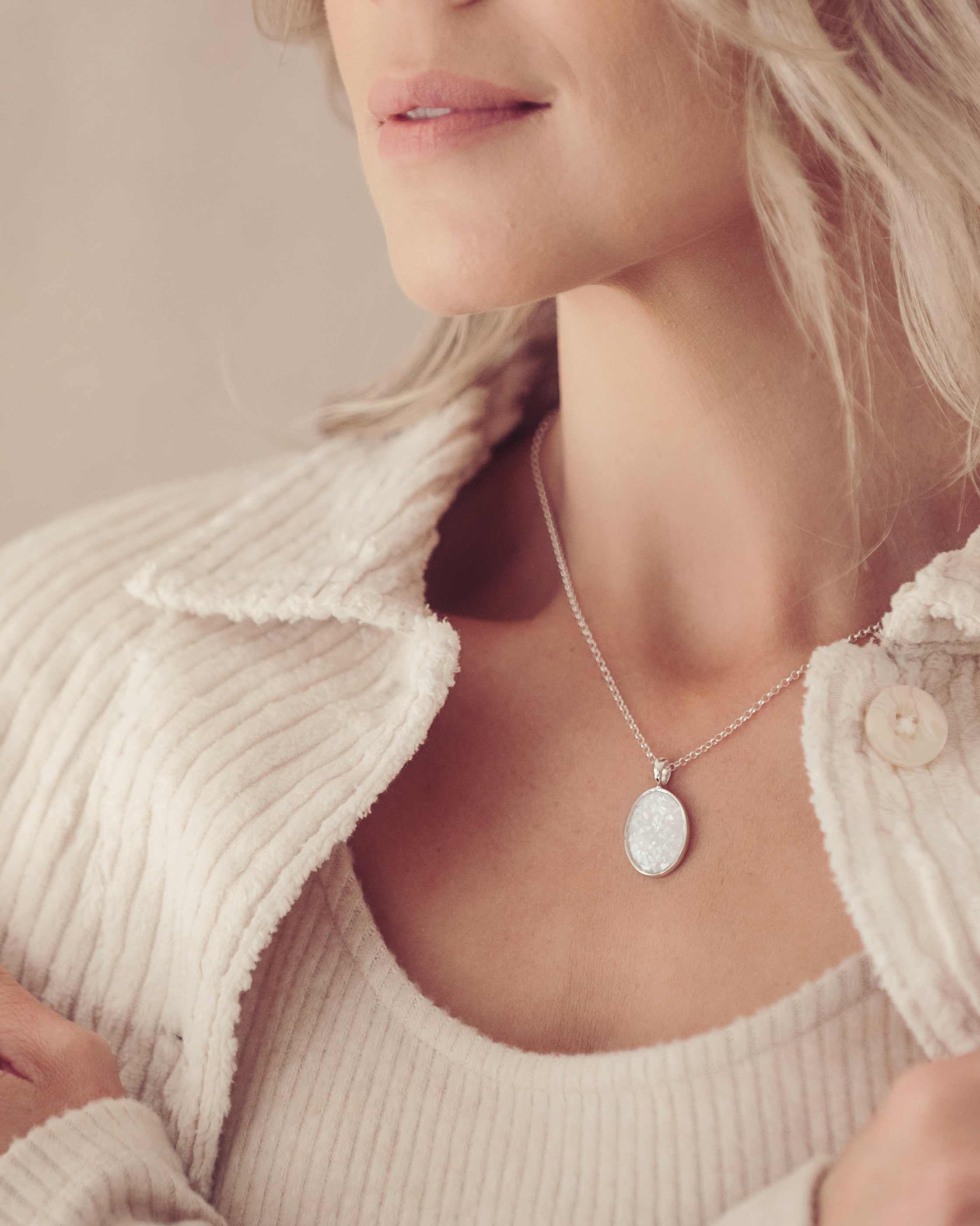 an image focussed on a blonde lady's neckline as she wears a silver oval necklace filled with cremation ashes