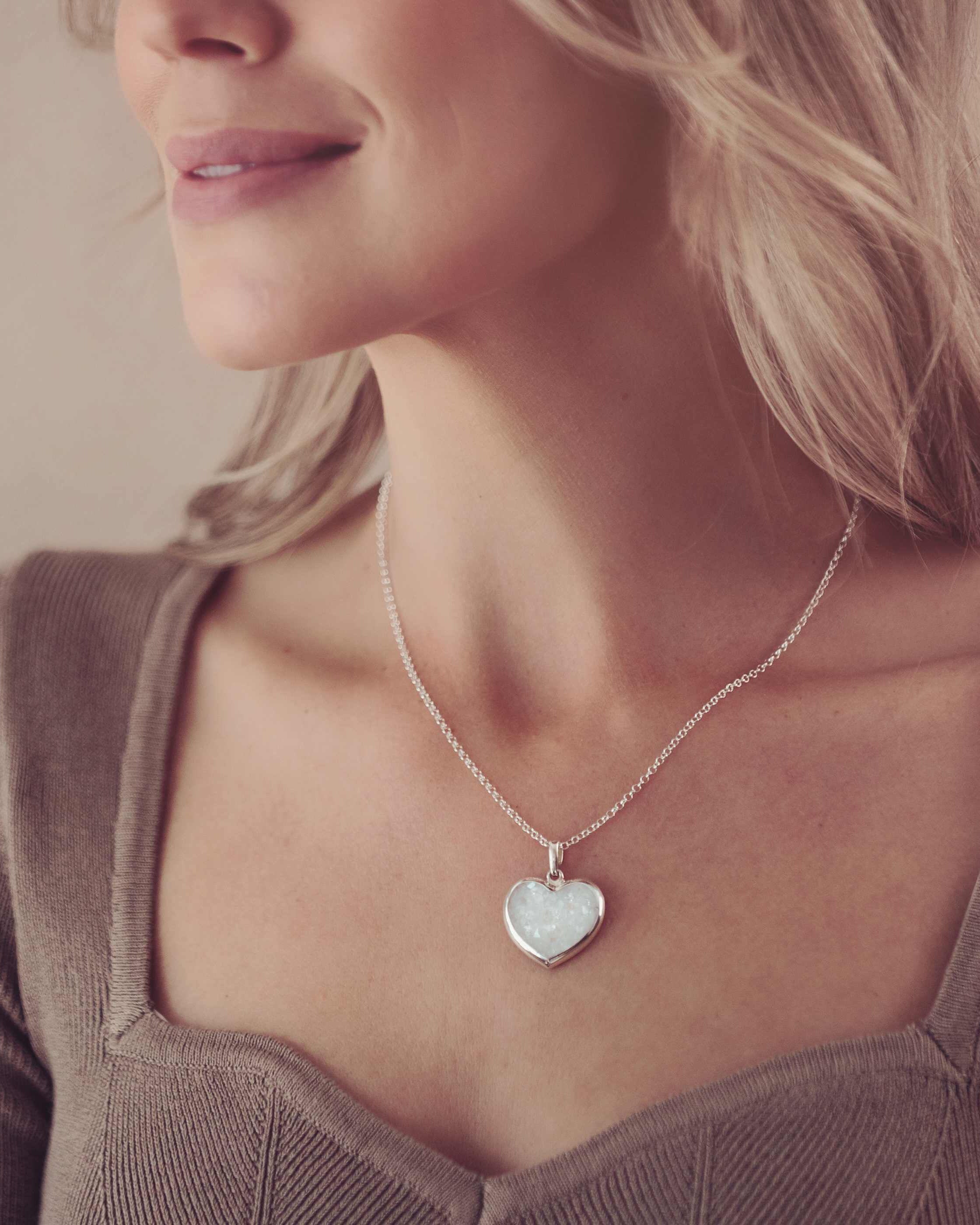A lady's neckline wearing a large silver necklace containing cremation ashes, the lady is wearing a brown top and has blonde hair