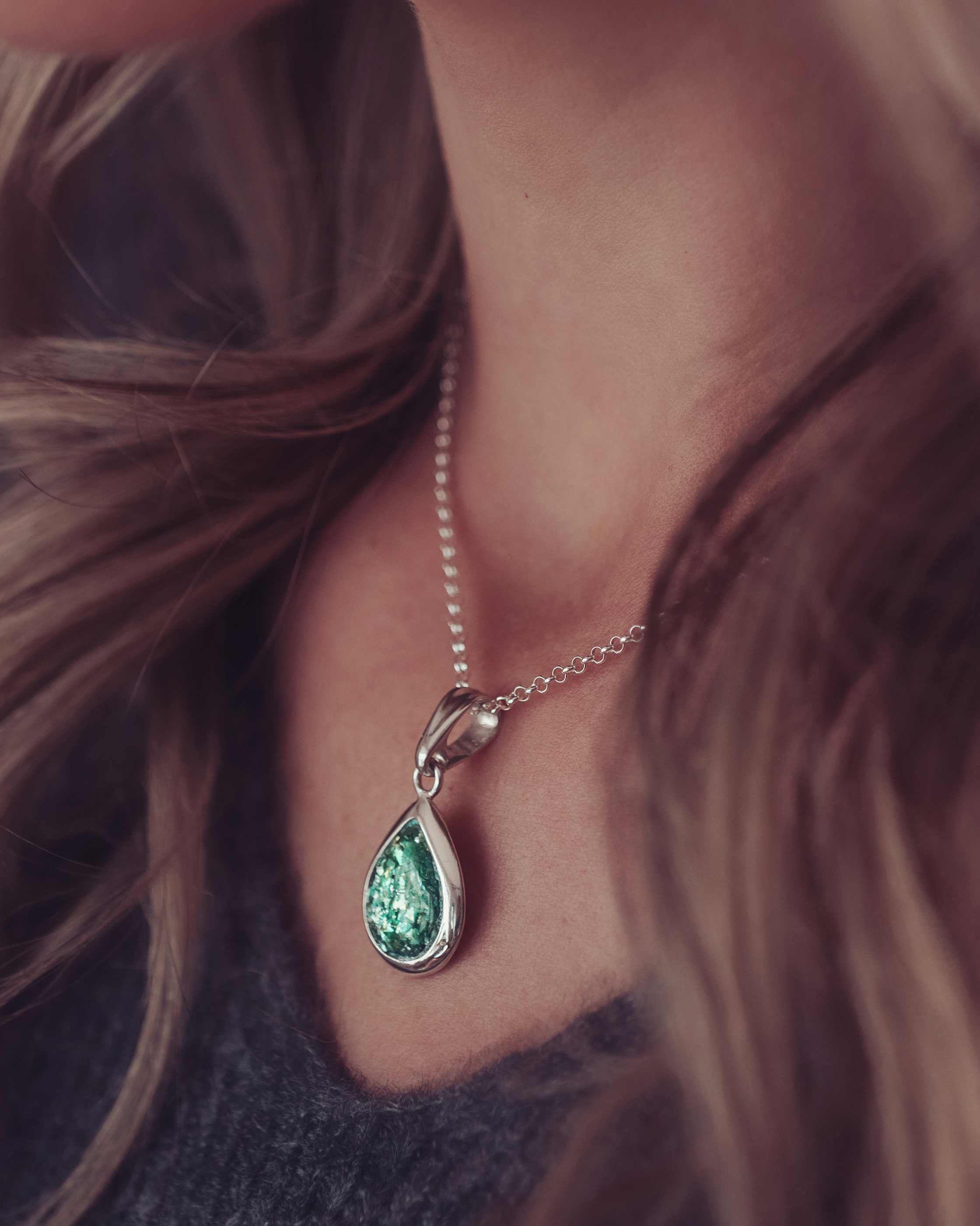A green ashes necklace being worn on a lady with long brown hair