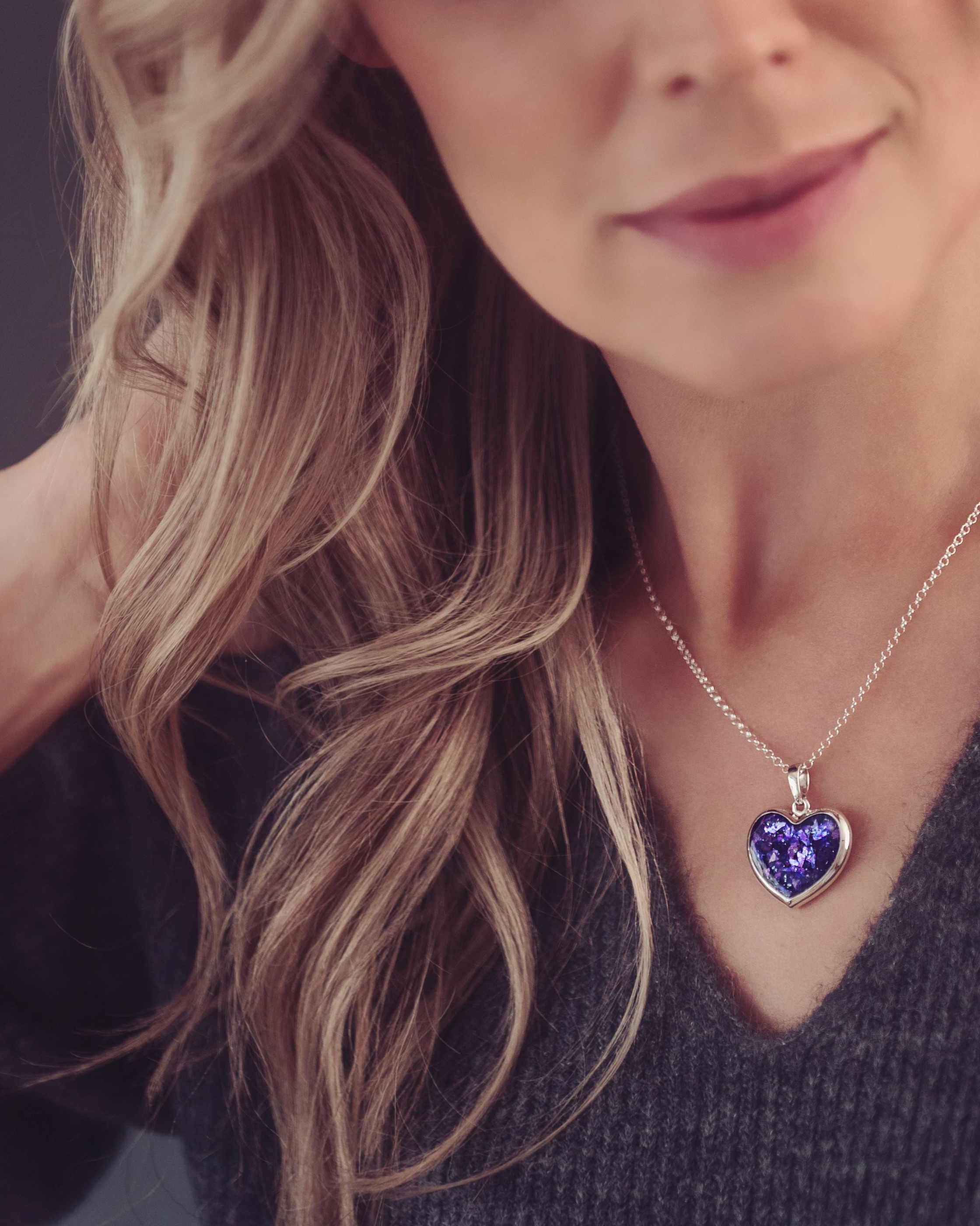 Lady with blonde hair wearing a grey knitted jumper and purple necklace filled with memorial cremation ashes