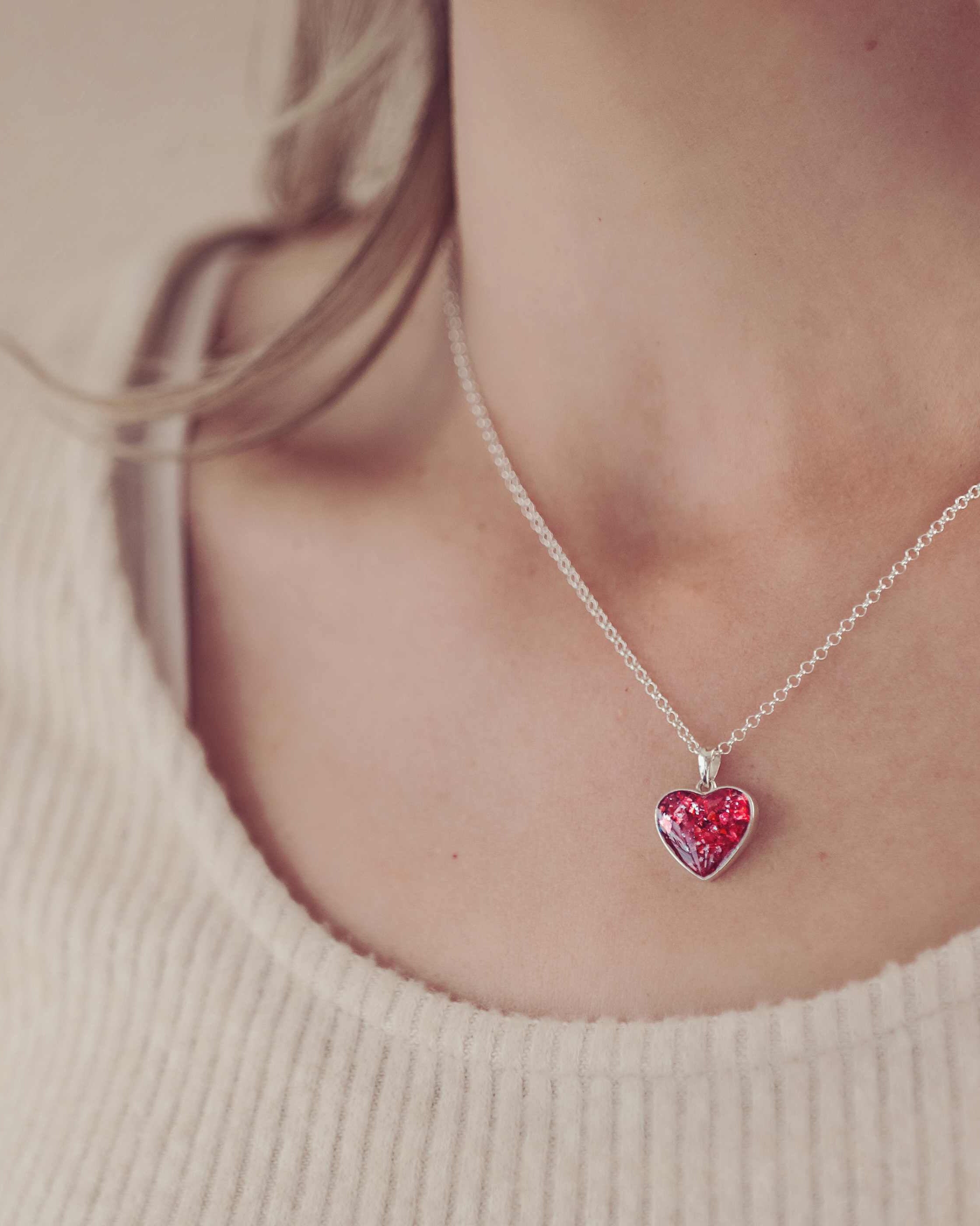 image of a lady's neckline while she's wearing a silver cremation ashes necklace in a red colour.