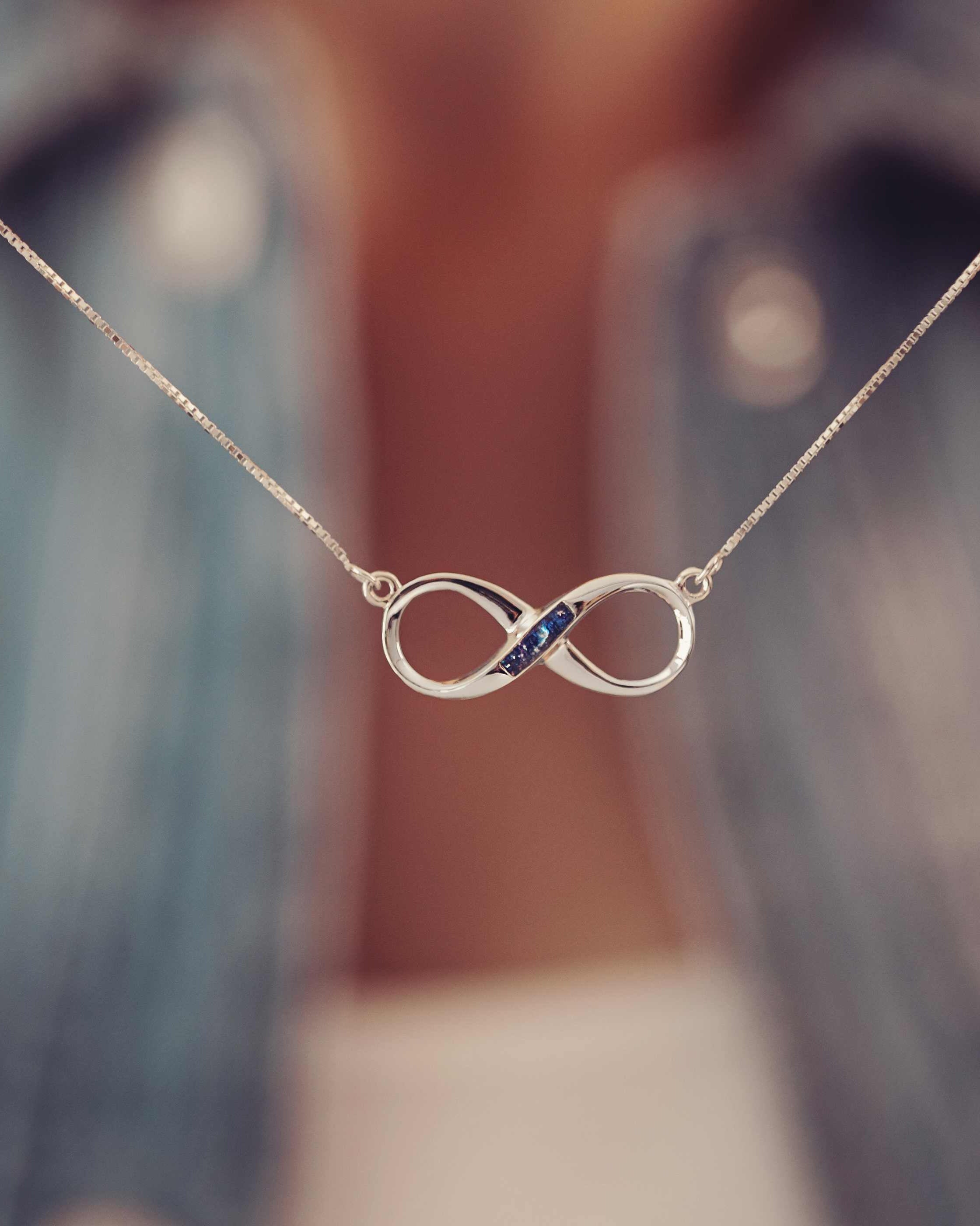 An infinity shaped necklace with a hollowed our section in the middle which is filled with deep blue cremation ashes