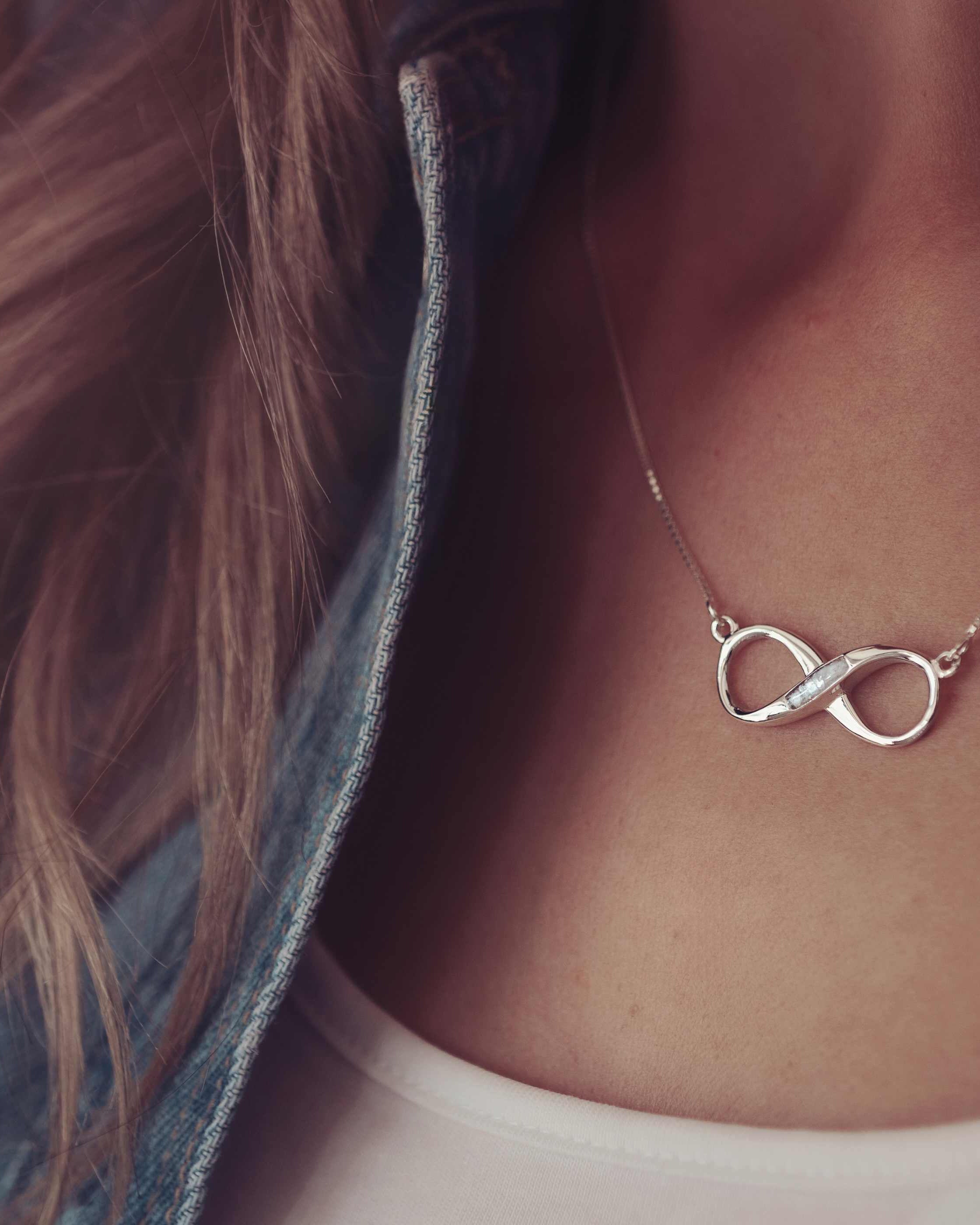 A silver infinity shaped necklace with the middle filled in with cremation ashes modelled on a lady.